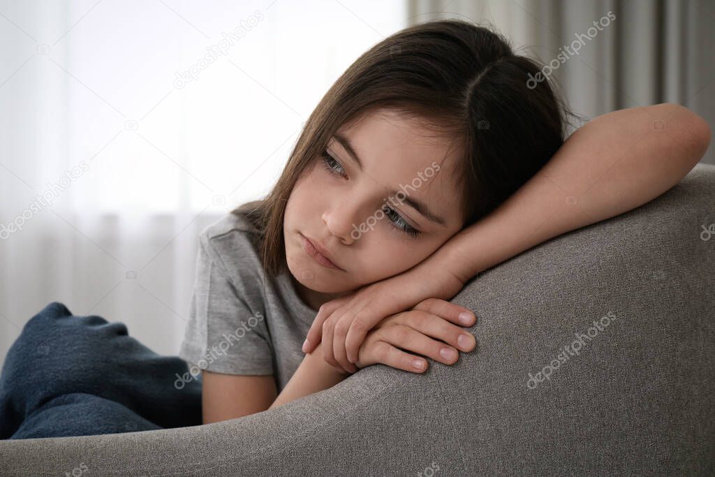 Sad little girl sitting on sofa indoors