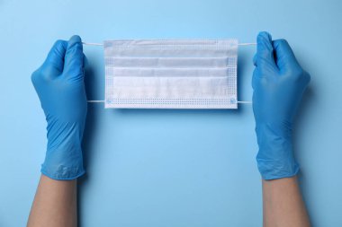 Açık mavi arka planda koruyucu maskeli bir kadın. Güvenlik ekipmanları