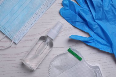 Koruyucu maskeler, tıbbi eldivenler ve beyaz ahşap arka planda antiseptik.