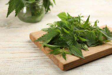 Beyaz ahşap masada taze ısırgan otu yapraklı tahta, yakın plan.