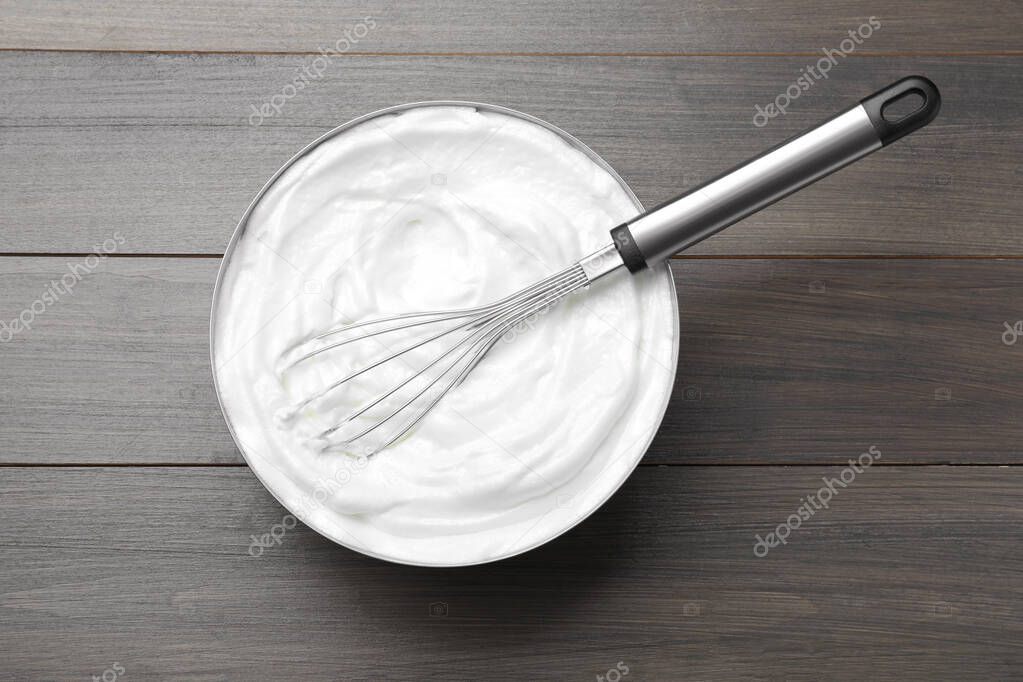 White cream with balloon whisk on grey wooden table, top view