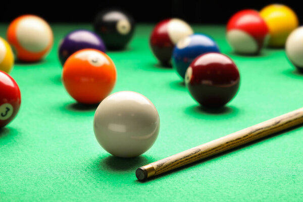 Many colorful billiard balls and cue on green table