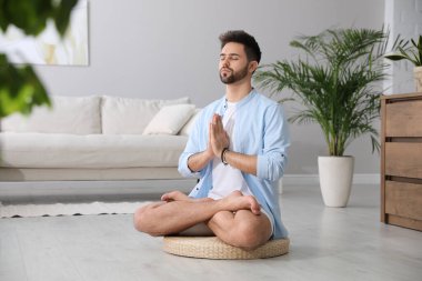Genç adam evdeki saman yastığında meditasyon yapıyor.