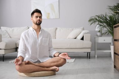Genç adam evde saman yastığı üzerinde meditasyon yapıyor, mesaj için yer var.