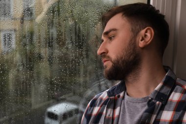 Depressed man near window at home. Space for text clipart