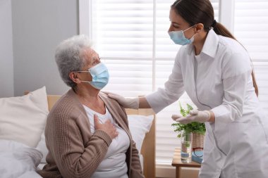 Doktor huzurevinde koruyucu maskeli yaşlı bir kadınla ilgileniyor.