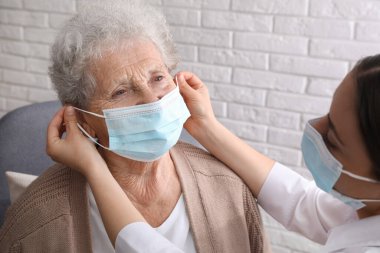 Doktor huzurevindeki yaşlı kadına koruyucu maske takıyor.