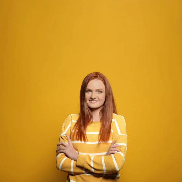 Candid portrait of happy young woman with charming smile and gorgeous red hair on yellow background