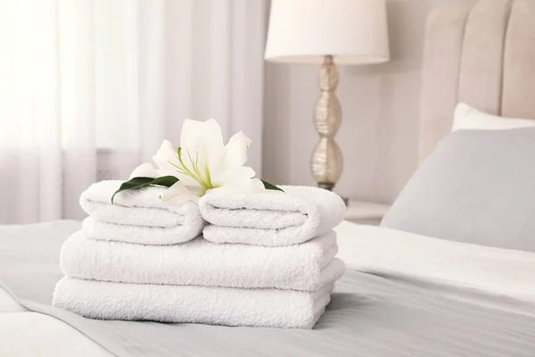 Stack of fresh towels with flower on bed indoors, space for text