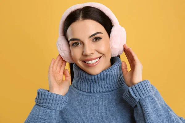 美しいです若いです女性身に着けていますEarmuff上の黄色の背景 — ストック写真