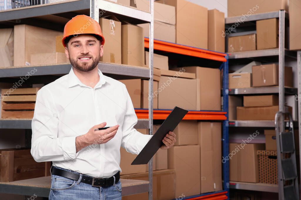 Young man with clipboard near rack of cardboard boxes at warehouse