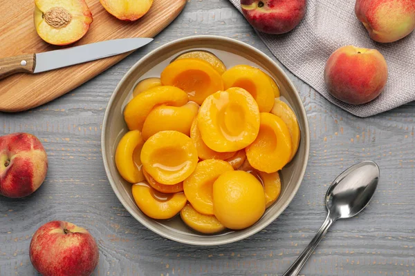 Canned peach halves on grey wooden table, flat lay