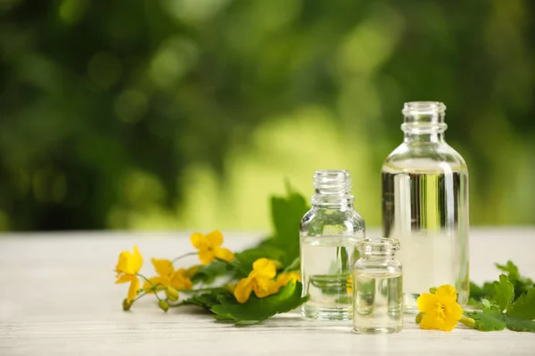屋外の白い木製のテーブルの上の花の近くに天然セランディン油のボトル テキストのためのスペース — ストック写真