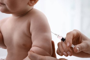 Doktor arka planda bebeğe aşı yapıyor, yakın plan. Sağlık hizmetleri