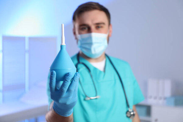 Doctor holding rubber enema in examination room, focus on hand. Space for text