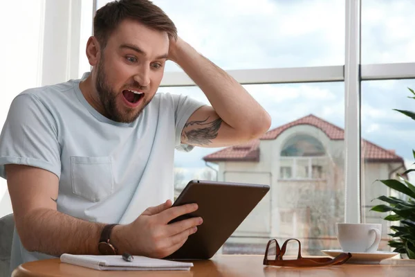 情绪激动的男人在家里用平板电脑参加网上拍卖 — 图库照片