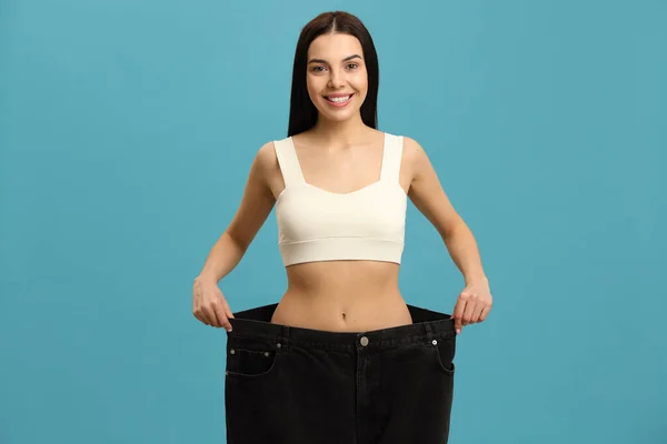 Glückliche Junge Frau Trägt Nach Gewichtsverlust Große Jeans Auf Türkisfarbenem — Stockfoto