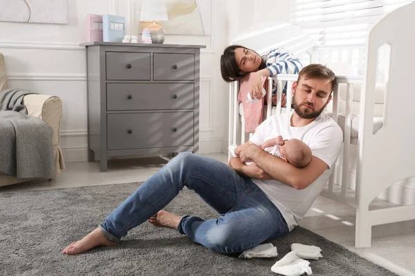 Tired young parents with their baby sleeping in children\'s room