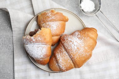 Lezzetli kruvasanlar ve açık gri masanın üzerine şeker tozu serpiştirilmiş düz kompozisyon