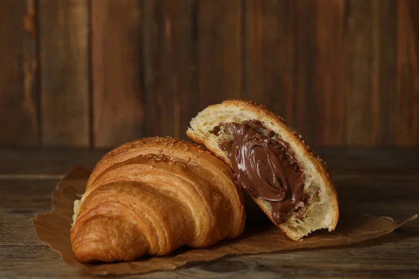 Tasty croissants with chocolate and sesame seeds on wooden table