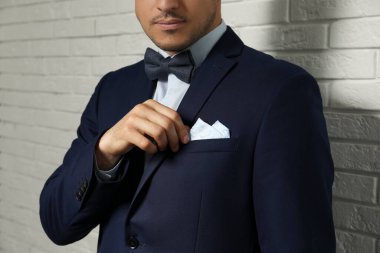 Takım elbisesinin göğüs cebinde beyaz tuğla duvarın yanında mendil tamir eden adam, yakın plan.