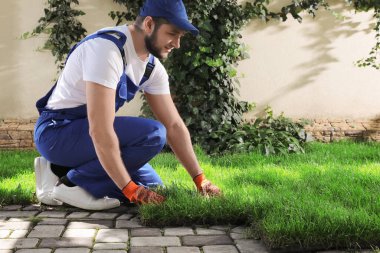 Üniformalı bahçıvan arka bahçeye çimen seriyor.