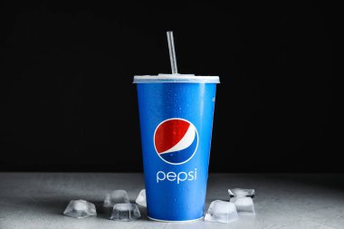 MYKOLAIV, UKRAINE - 9 Haziran 2021: Koyu arkaplana karşı açık gri masada kağıt Pepsi bardağı ve buz küpleri