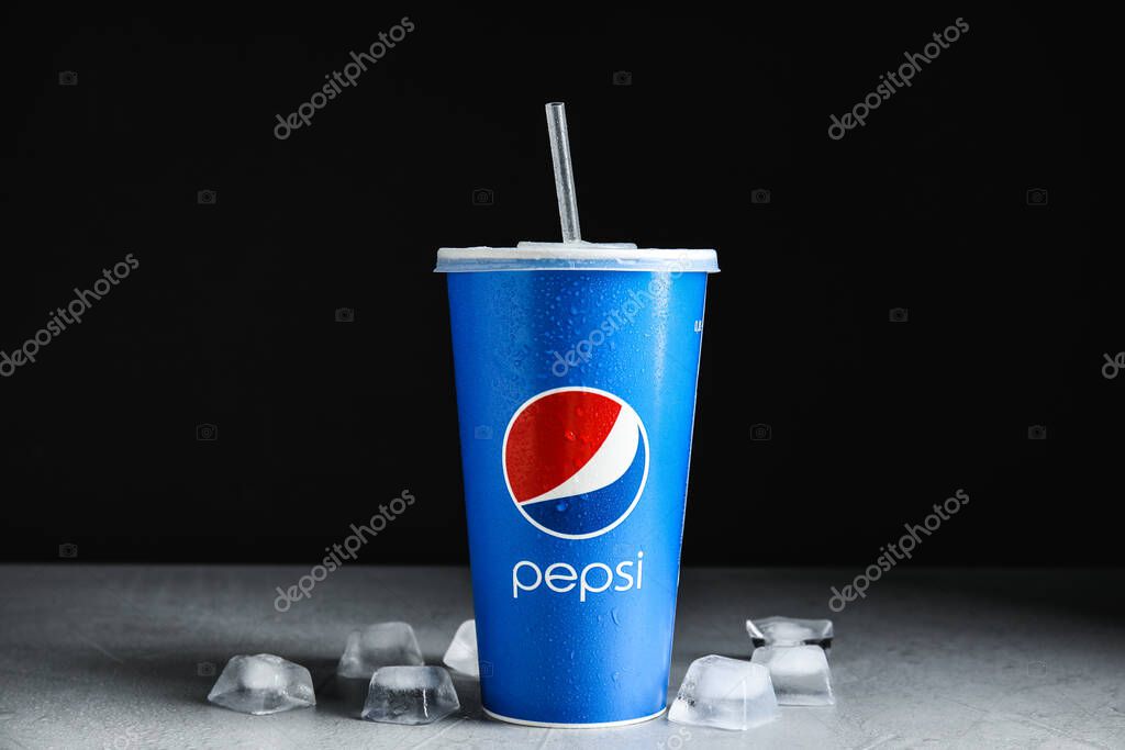 MYKOLAIV, UKRAINE - JUNE 9, 2021: Paper Pepsi cup and ice cubes on light grey table against dark background