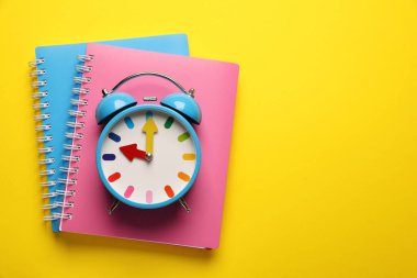 Alarm saati ve sarı arka planda not defterleri, üst manzara. Metin için boşluk