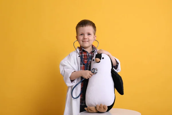 可愛いです男の子で小児科医の制服遊びとともにStethoscopyとおもちゃペンギン上の黄色の背景 — ストック写真