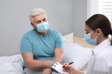 Doktor huzurevinde koruyucu maskeli yaşlı adamı muayene ediyor.