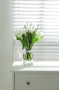 Pencerenin yanındaki vazoda söğüt dalları ve laleler.