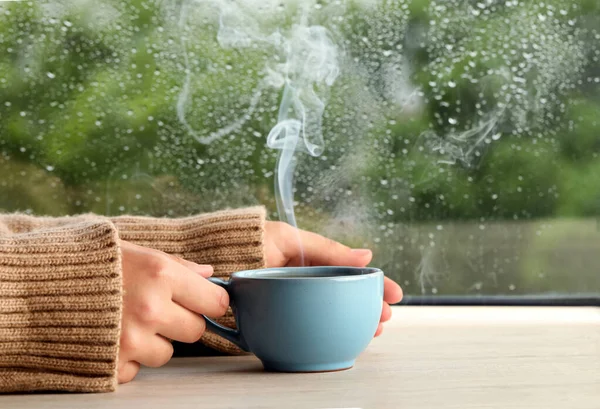 Frau Mit Tasse Heißgetränk Holztisch Neben Fenster Regnerischem Tag Nahaufnahme — Stockfoto