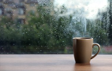 Yağmurlu bir günde pencerenin yanında bir fincan sıcak içecek. Metin için boşluk