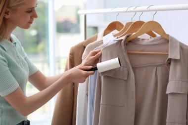 İç mekanda pamuklu bezle giysileri temizleyen genç bir kadın, yakın plan.