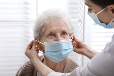 Doktor huzurevindeki yaşlı kadına koruyucu maske takıyor.