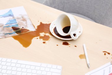 Bir fincan çay tabağı ve ahşap ofis masasına dökülmüş kahve.
