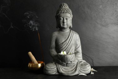 Buda heykeli siyah masanın üzerinde şarkı söyleyen kasenin yanında.