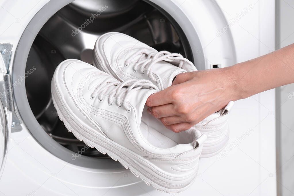 Woman putting pair of sport shoes into washing machine, closeup