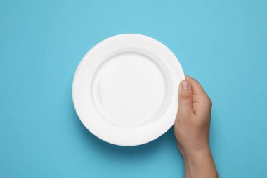 Açık mavi arkaplanda boş tabak tutan adamın üst görünümü, yakın plan