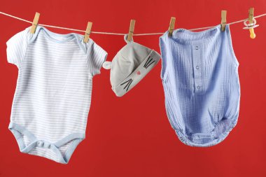 Bebek kıyafetleri kırmızı arka planda çamaşır ipine asılı.