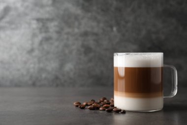 Cam bardakta sütlü sıcak kahve ve gri masada fasulye. Metin için boşluk