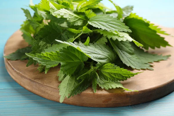 Träskiva Med Färska Brännässlor Blad Ljusblått Bord Närbild — Stockfoto