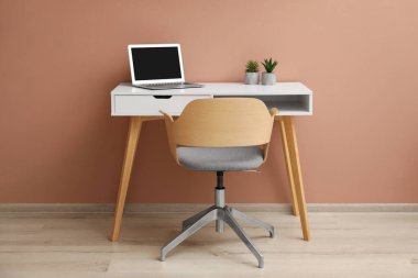 Bilgisayarlı şık bir iş yeri ve kapalı alanda bej duvarın yanında rahat bir sandalye. İç tasarım