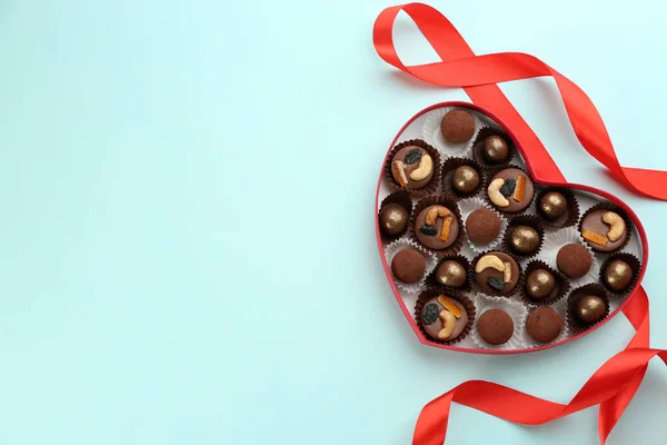 不同的美味巧克力糖果在心形盒和带浅蓝色背景 顶部视图 案文的篇幅 — 图库照片
