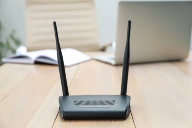 Modern Wi-Fi yönlendirici ahşap masada, bilgisayarla kapalı alanda.