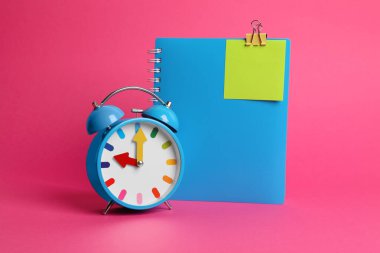 Alarm saati ve pembe arkaplan üzerinde boş hatırlatma notu olan defter, metin için boşluk