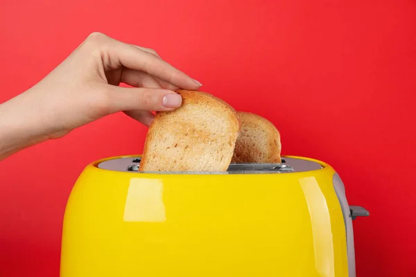 Vrouw Neemt Brood Slice Uit Broodrooster Rode Achtergrond Closeup — Stockfoto