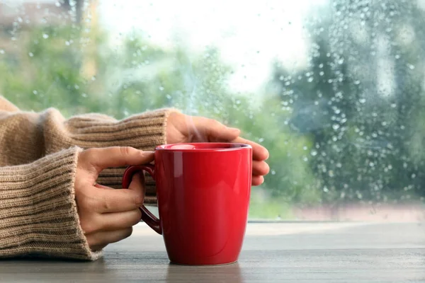 Frau Mit Tasse Heißgetränk Holztisch Neben Fenster Regnerischem Tag Nahaufnahme — Stockfoto