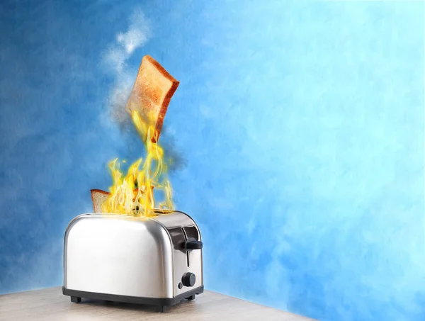 烤面包机在用蓝色背景的白色木制桌子上烤着几片面包时燃烧起来 不安全器具 — 图库照片